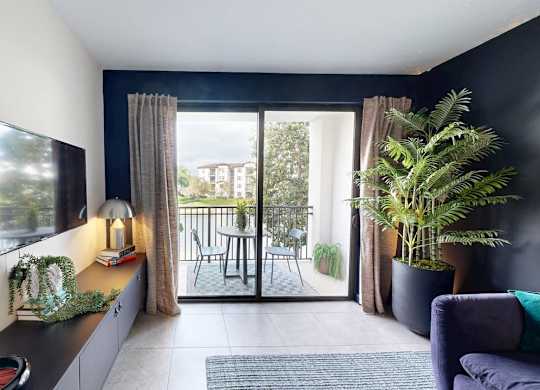 A living room with a flat screen TV on the wall and a sliding glass door leading to a balcony.
