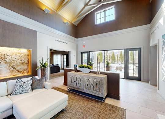 A white sofa with grey pillows is in the middle of a room with a wooden floor and a brown wall.