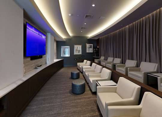 A row of white chairs are lined up in a room with a blue screen on the wall.