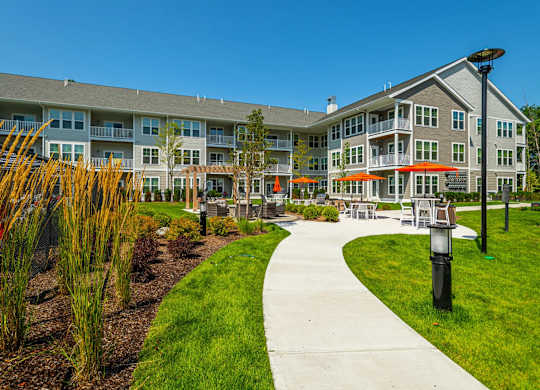 A walkway leads to a building with a grassy area and trees in the foreground.