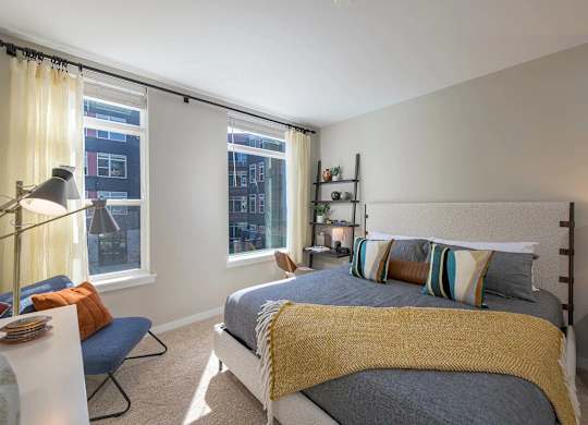 A bedroom with a bed, a chair, and a window with curtains.
