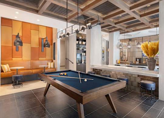 A pool table is in the middle of a room with a bar and a couch.