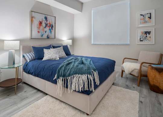 A bedroom with a bed, chair, and artwork on the wall.