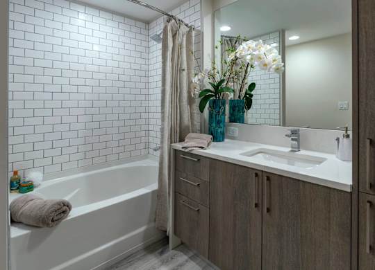 A white tiled bathroom with a white tub and a white sink.