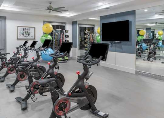 A room with a row of stationary bikes and a television.