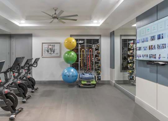 A gym with exercise equipment and a wall-mounted TV displaying fitness-related images.