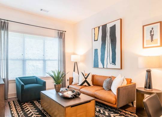 A living room with a brown couch, a blue chair, and a painting on the wall.