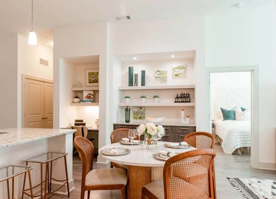 A dining room with a table set for two and a kitchen area in the background.
