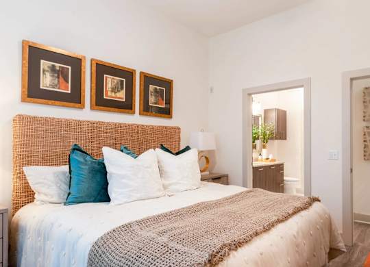 A bedroom with a bed, pillows, and pictures on the wall.