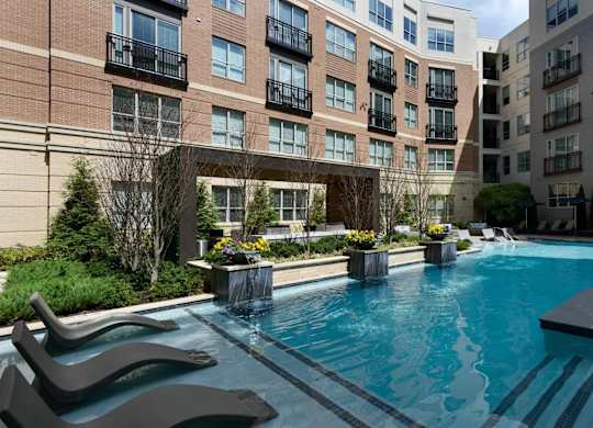 A swimming pool surrounded by a black bench and a building in the background.