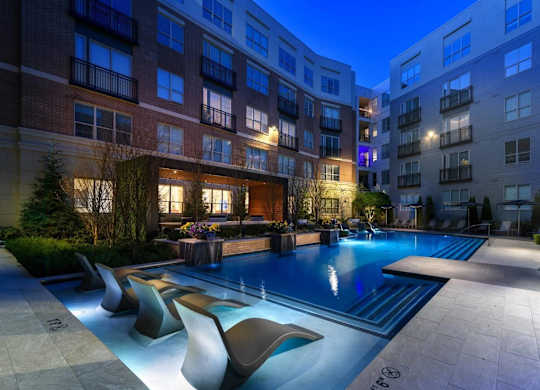 A swimming pool surrounded by lounge chairs in front of apartment buildings.