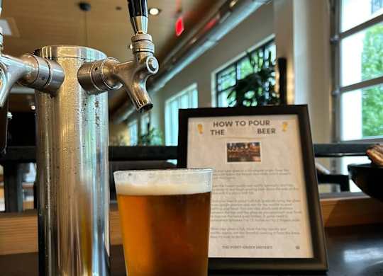 A glass of beer is on a metal stand with a sign that says