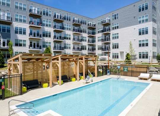 A large swimming pool is surrounded by sun loungers and a wooden pergola.