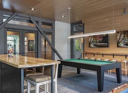 A pool table is in the middle of a room with a bar and a television.