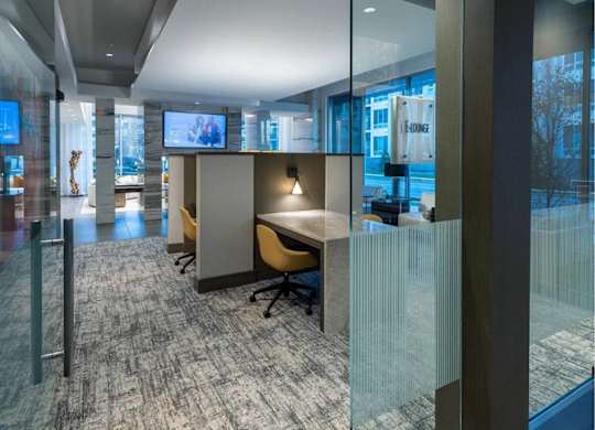 A modern office space with glass partitions and a grey carpet.
