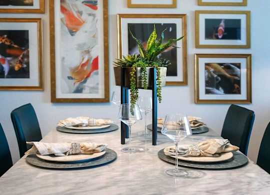A dining table set with plates and glasses in front of a wall with framed pictures.