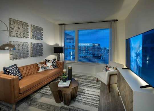 A living room with a brown couch, a coffee table, and a large window with blinds.