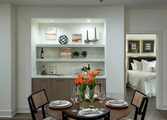 A dining room with a table set for two and a bed in the background.