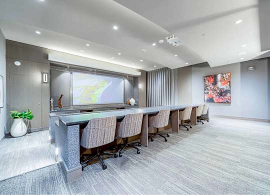 A conference room with a long table and chairs, a screen, and a plant.