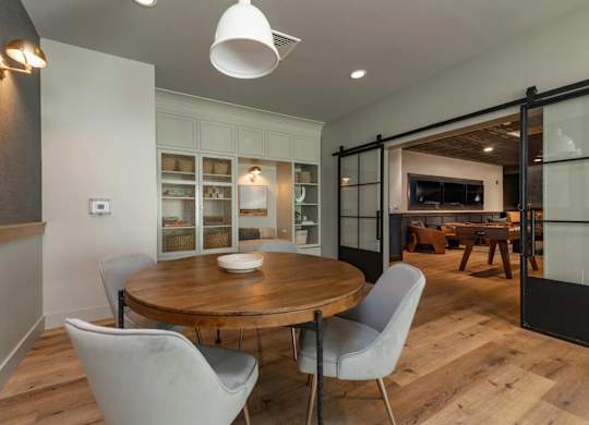 A modern dining room with a round wooden table and four grey chairs.