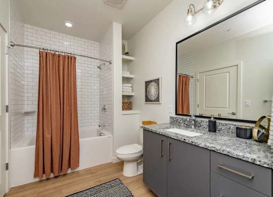 A bathroom with a brown shower curtain and a white tiled shower.