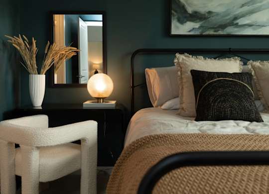 A bedroom with a bed, chair, and a painting on the wall.