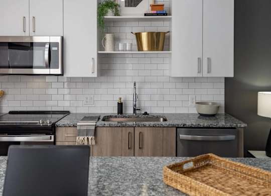 A laptop is open on a kitchen counter with a basket beside it.