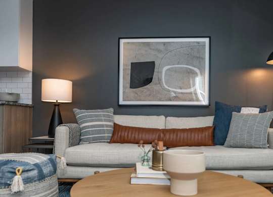A modern living room with a grey couch, a coffee table, and a large abstract painting on the wall.