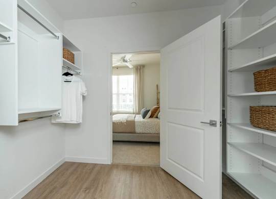 A white closet with clothes hanging and a basket on the shelf.