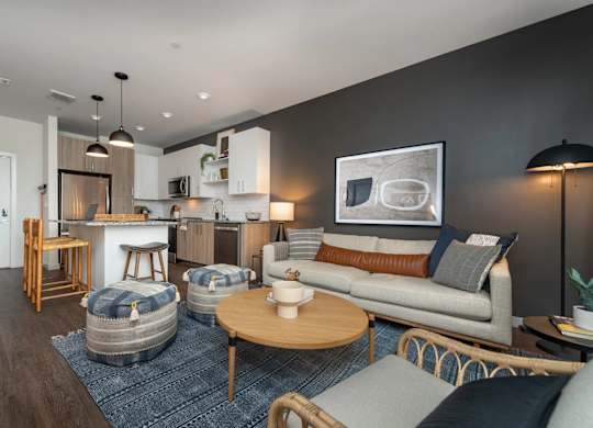 A modern living room with a grey couch, a wooden coffee table, and a kitchen area in the background.