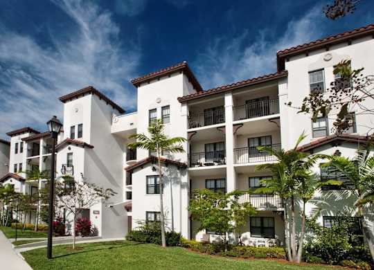 A white apartment building with balconies and trees in front.