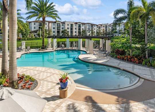 A large outdoor swimming pool surrounded by palm trees and a building in the background.