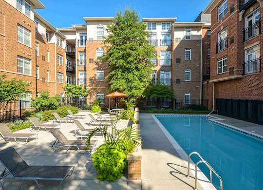 A pool surrounded by chairs and plants in front of apartment buildings.