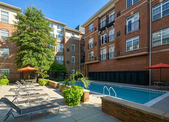 A pool surrounded by a brick building and lounge chairs.