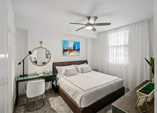 A bedroom with a bed, desk, chair, and a ceiling fan.
