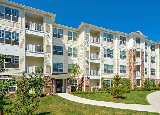 A large white apartment building with balconies and a green lawn in front.