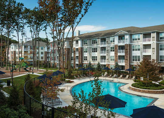 A large swimming pool surrounded by trees and chairs in front of apartment buildings.