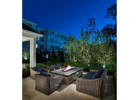 A patio with a fire pit surrounded by chairs and plants.