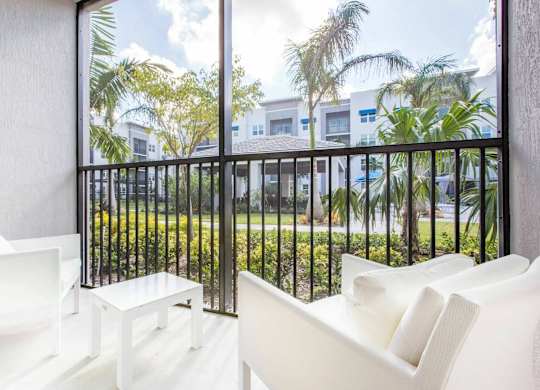 A white chair is in front of a balcony with a view of a green lawn and trees.
