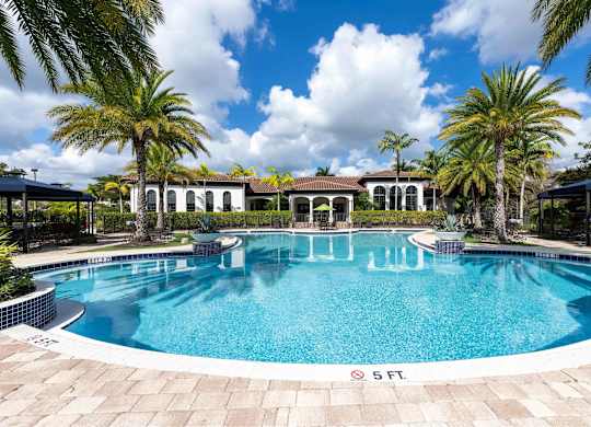 A large swimming pool surrounded by palm trees and a building in the background.