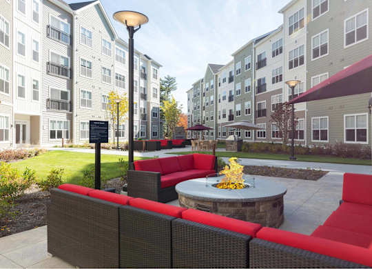 A patio with red couches and a fire pit in front of apartment buildings.
