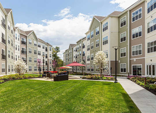 A sunny day at a well-maintained apartment complex with a grassy courtyard and a red umbrella.