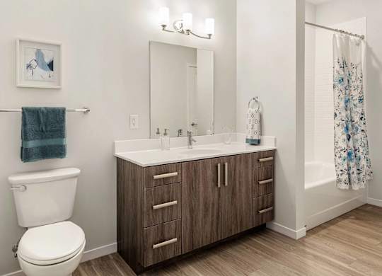 A bathroom with a white toilet, a wooden vanity with a mirror, and a shower with a floral shower curtain.
