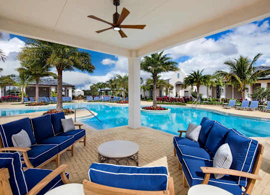 A poolside patio with blue couches and a ceiling fan.