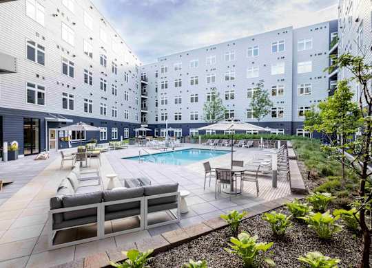 A pool surrounded by a patio with chairs and a bench.