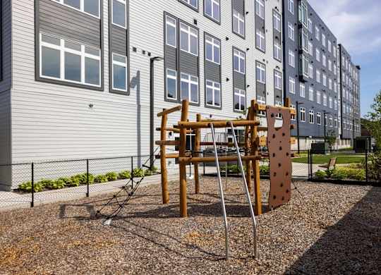 A playground with a wooden swing set in front of a grey apartment building.