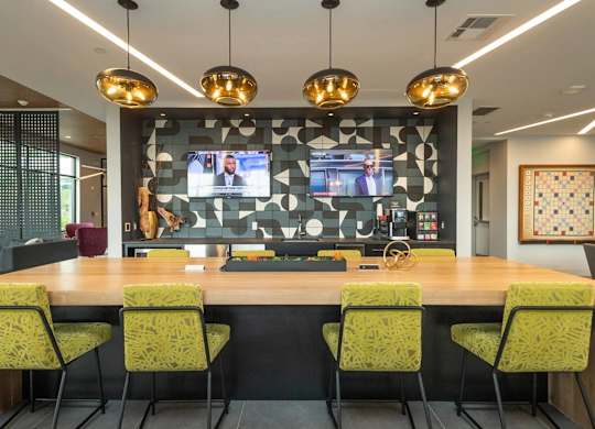 A conference room with a long table and chairs, a television screen, and hanging lights.