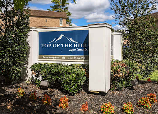 A sign for Top of the Hill Apartments is shown in front of a building.