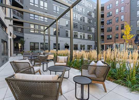 A patio with chairs and tables is surrounded by buildings.