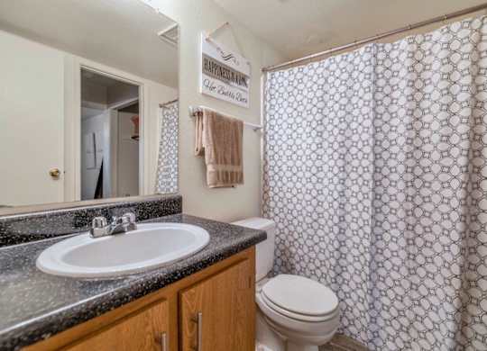 A bathroom with a toilet, sink, and shower curtain at Reflections at Red Mountain Apartments, Arizona, 85213